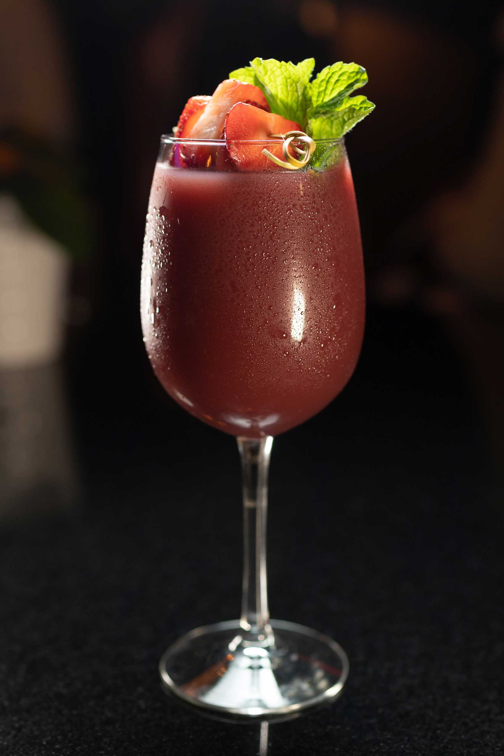 A rich and elegant berry-infused cocktail served in a sleek wine glass, garnished with freshly sliced strawberries and a sprig of vibrant mint. The deep red hue of the drink glistens under the soft lighting, with delicate condensation on the glass adding a refreshing touch. Perfectly embodying the high-quality diner food experience, this beverage is a standout offering at NYC’s top-rated diners. Ideal for late-night dining in Manhattan or as an accompaniment to comfort food favorites, this cocktail highlights the creativity of NYC's 24/7 diners and affordable comfort food spots.